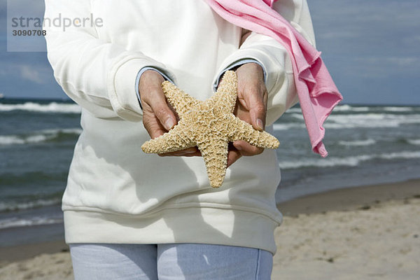 Eine ältere Frau mit einem Seestern am Strand  Mittelteil