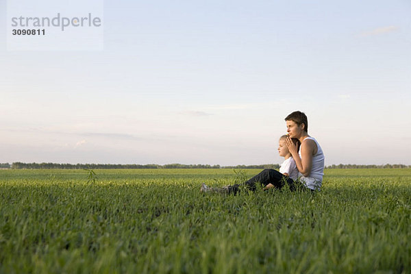 Seitenansicht einer Frau und eines Mädchens  die zusammen auf einem Feld sitzen