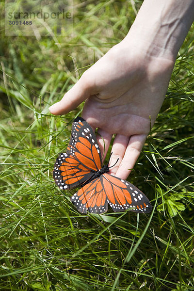 Eine Hand mit einem künstlichen Monarch-Schmetterling