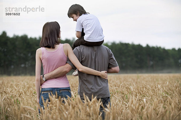 Eine junge Familie  die durch ein Weizenfeld läuft.