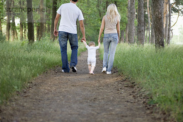 Zwei Eltern  die mit ihrer kleinen Tochter auf einem Waldweg spazieren gehen.