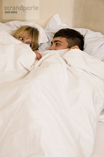 Ein junges Paar im Bett mit hochgezogener Bettdecke
