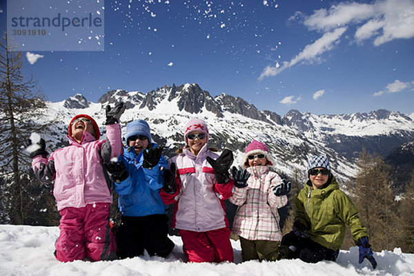 5 Kinder  die kniend Schnee werfen.