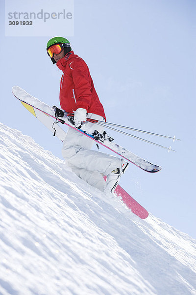 Mann sündigt rot und trägt Skier bergauf.