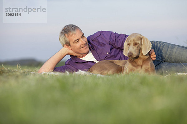 Mann mit Hund lächelnd auf dem Gras liegend