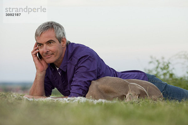 Mann mit Hund am Telefon im Gras