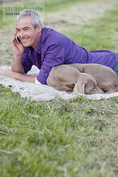 Mann mit Hund am Telefon im Gras