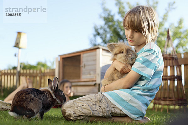 Junge spielt mit Kaninchen im Garten