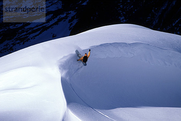 Snowboarder dreht sich um eine Schneebank.