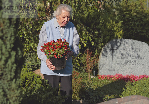Seniorin bringt auf Friedhof Blumen an Grab