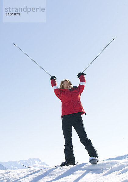 Seniorin auf Skiern  streckt Skistöcke in die Luft