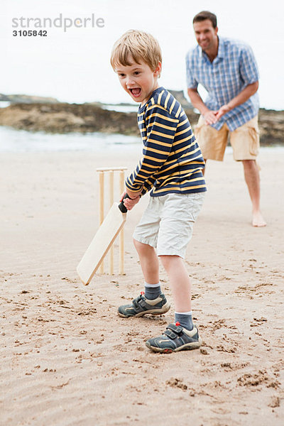 Vater und Sohn spielen Cricket am Strand