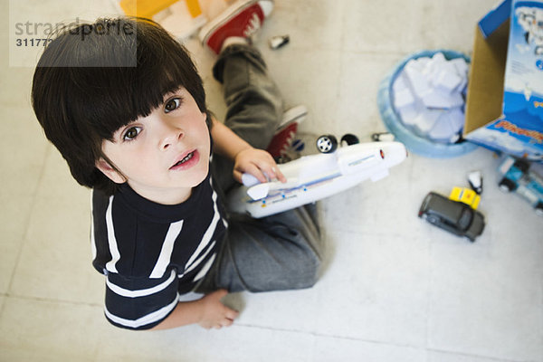 Kleiner Junge sitzt auf dem Boden  spielt mit Spielzeug und schaut in die Kamera.