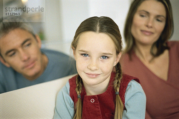 Kleines Mädchen lächelt in die Kamera  Eltern im Hintergrund