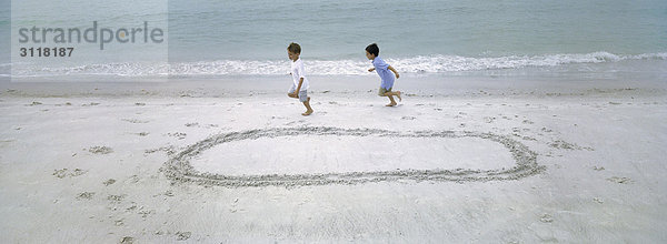 Jungen  die am Strand rennen und sich gegenseitig um den im Sand gezogenen Kreis jagen.