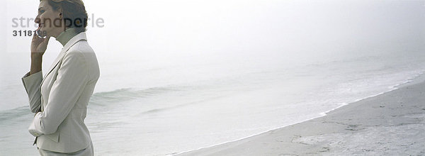 Frau am Strand mit dem Handy  bewundernde Aussicht