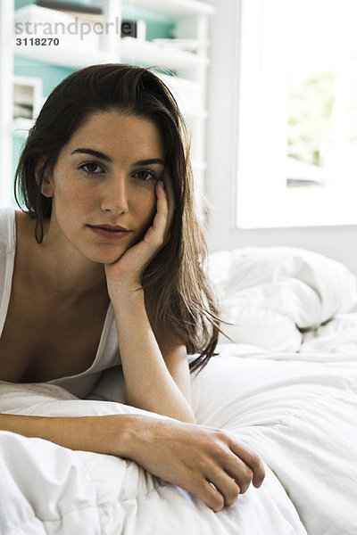 Frau auf dem Bett liegend  auf den Ellenbogen gestützt  mit Blick auf die Kamera