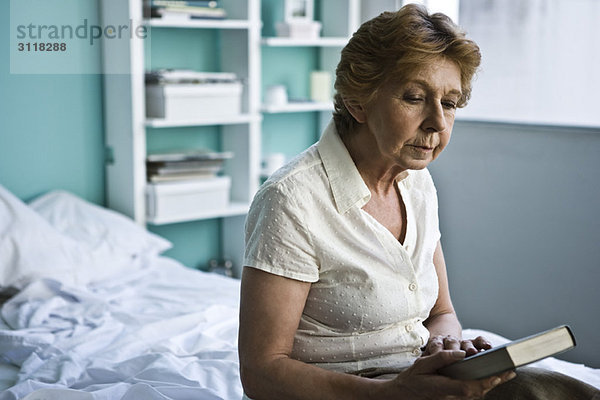 Seniorin sitzend im Schlafzimmer mit Blick auf das Buch