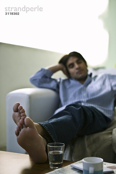 Mann auf Sofa sitzend mit Füßen oben auf dem Couchtisch