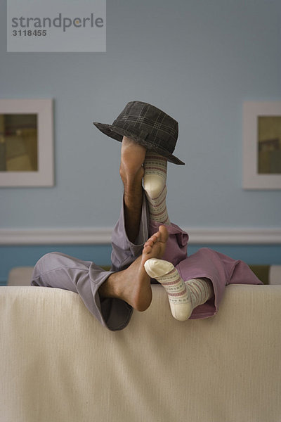 Zwei Personen auf dem Sofa liegend  Beine hochgeklappt  Hut auf Füße gesetzt  Rückansicht