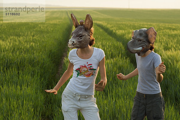 Zwei Weibchen mit Tiermasken  die auf dem Feld tanzen.