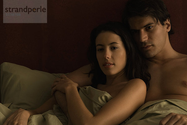 Paar liegt zusammen im Bett  der Arm des Mannes um die Schulter der Frau.
