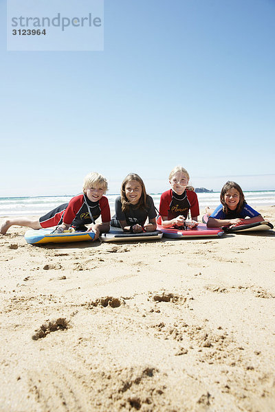 Kinder mit Surfbrettern am Strand liegend  Frontal