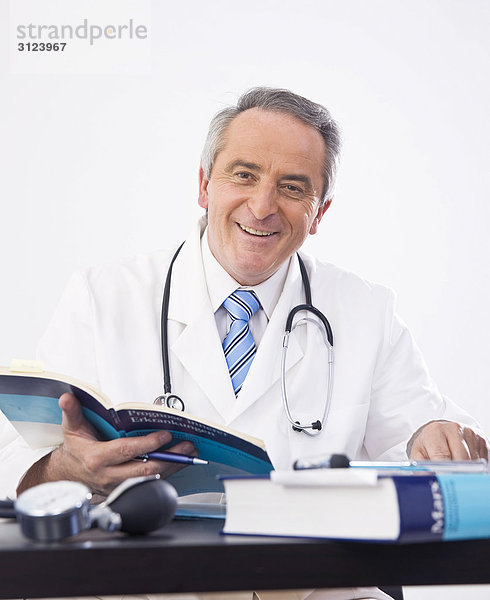 Arzt sitzend am Schreibtisch mit einem Buch in der Hand  Porträt