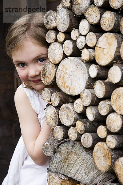 Ein Mädchen  das sich hinter Baumstämmen versteckt.