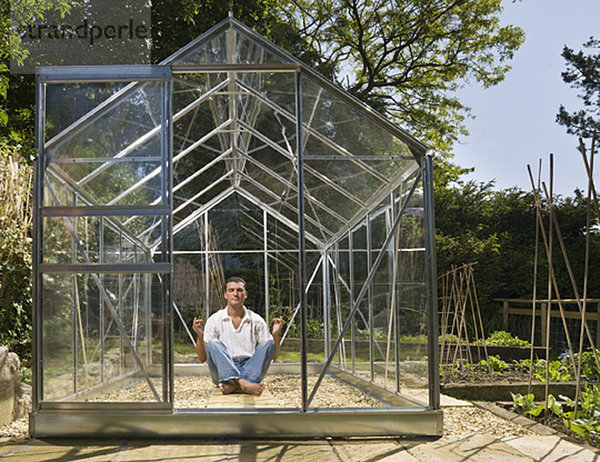 Mann meditiert im Gewächshaus im Garten