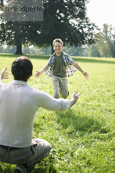 Ein Sohn  der zu seinem Vater im Park rennt.