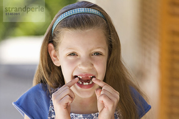 Ein junges Mädchen zeigt auf ihre fehlenden Zähne.
