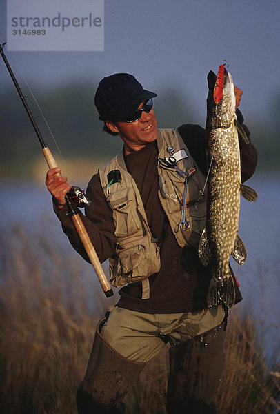 Angler hält eine Rute und einen Fisch.