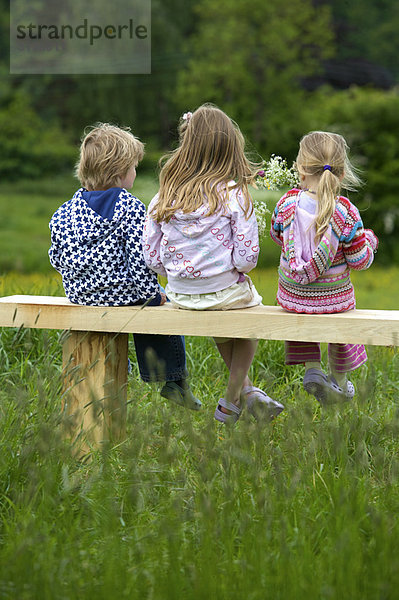 3 Kinder sitzen auf einer Bank.