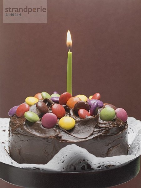 Schokoladentorte mit bunten Schokolinsen und Kerze