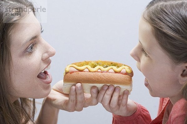 Frau und Mädchen gemeinsam an beiden Enden einen Hot Dog essend