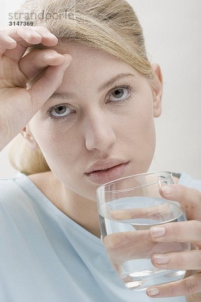 Frau mit Kopfweh trinkt Glas Wasser