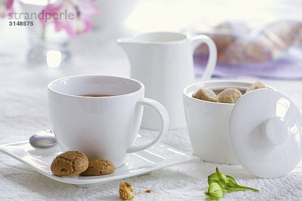 Eine Tasse Tee mit Zuckerdose  Milchkännchen und Keksen