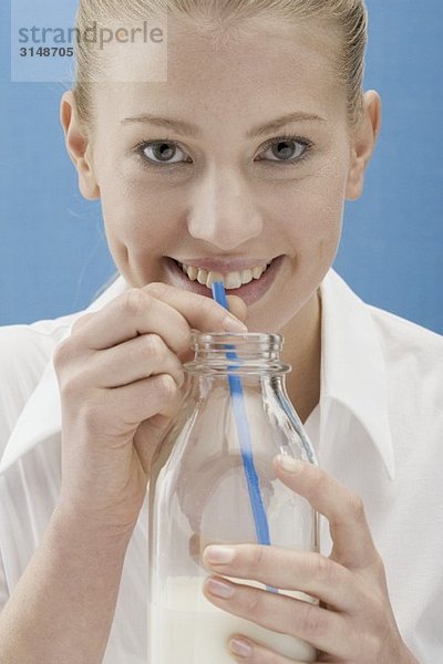 Junge Frau trinkt Milch mit Strohhalm aus der Flasche