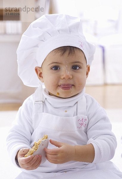 Kleines Mädchen mit Kochmütze isst Plätzchen