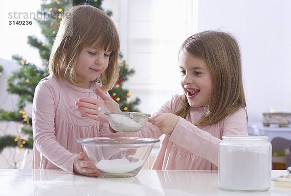 Weihnachtsbäckerei: Zwei Mädchen sieben Puderzucker