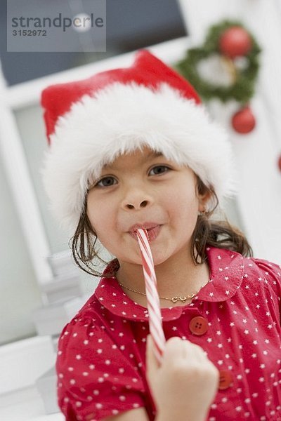 Kleines Mädchen mit Nikolausmütze isst Zuckerstange