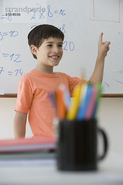Grundschüler steht vor der Klasse und zeigt auf das Whiteboard.