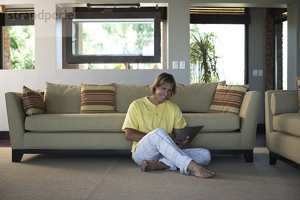 Mann sitzt auf dem Boden des Wohnzimmers mit dem Laptop