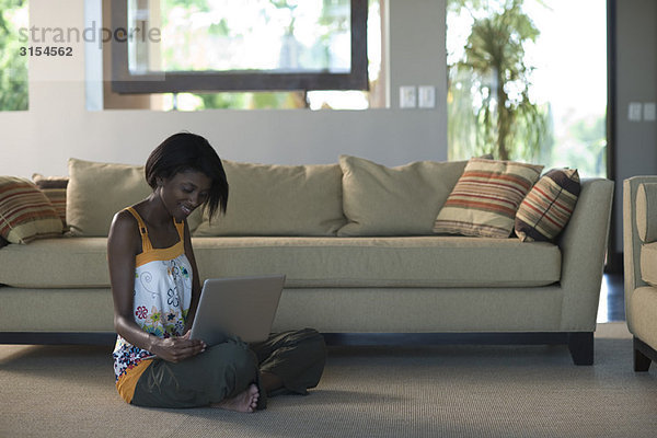 Junge Frau sitzt auf dem Boden des Wohnzimmers mit dem Laptop