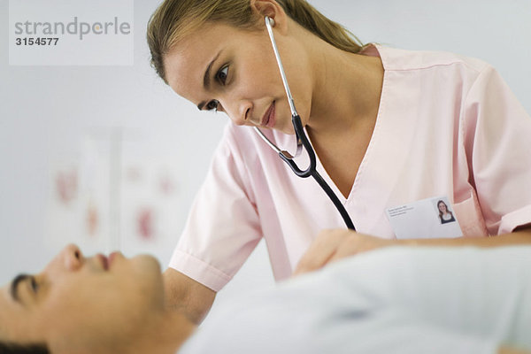 Krankenschwester hört mit Stethoskop auf die Brust des Patienten