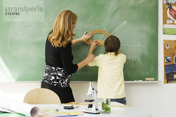 Lehrer hilft dem Jungen beim Zeichnen des Winkels auf der Tafel mit dem Winkelmesser  Rückansicht