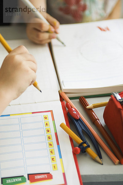Kinder schreiben in Notizbücher  Schulsachen in der Nähe  beschnitten