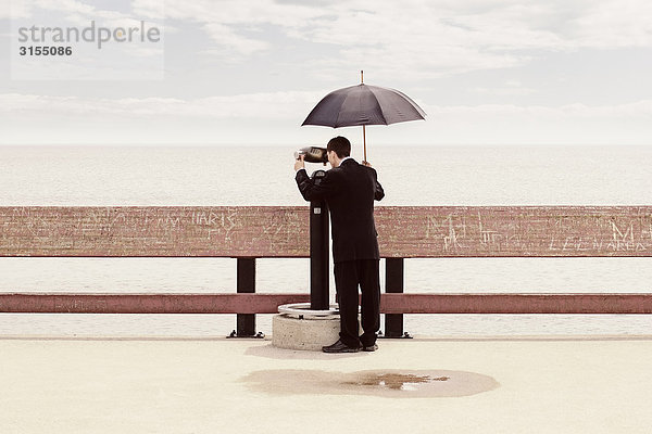 Man in suit holding umbrella  looking through binoculars