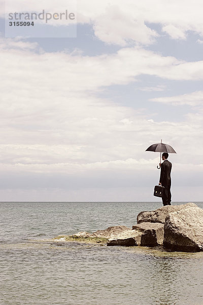 Man in suit holding umbrella and briefcase standing on breakwater